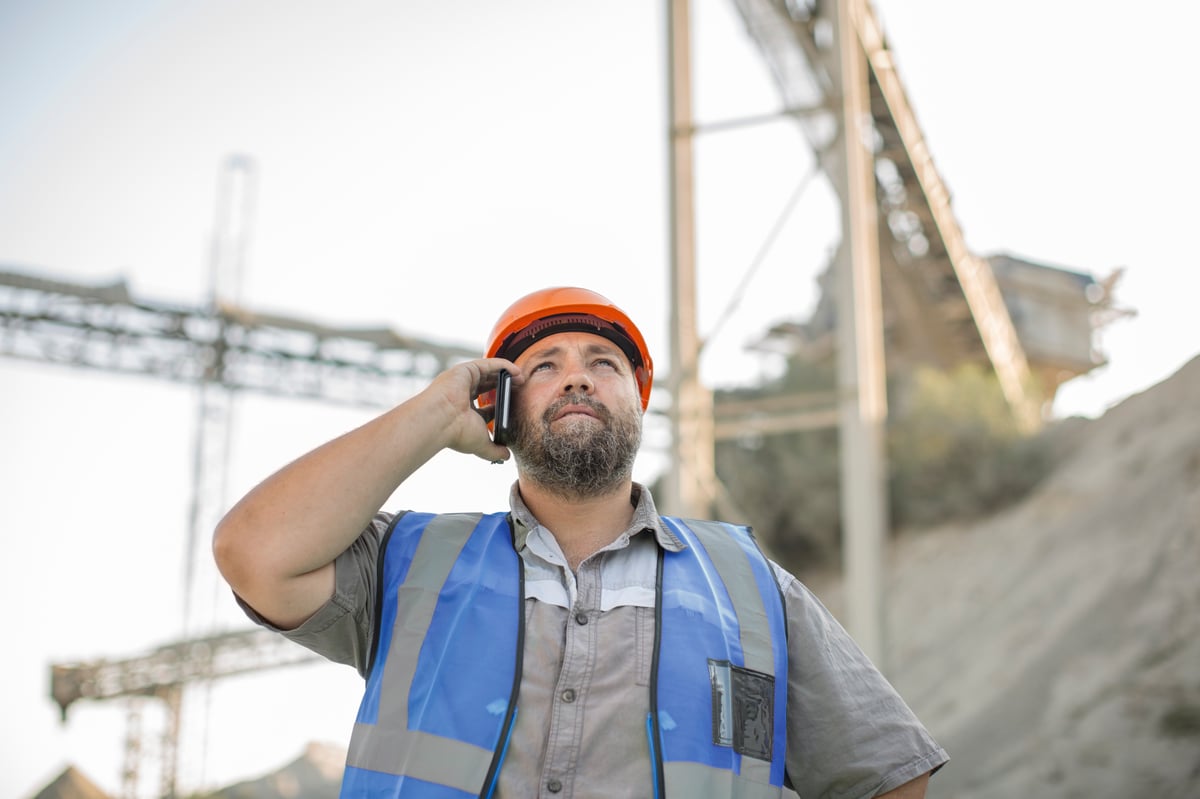 quarry-worker-in-quarry-using-smartphone-looking-2022-03-08-00-15-03-utc